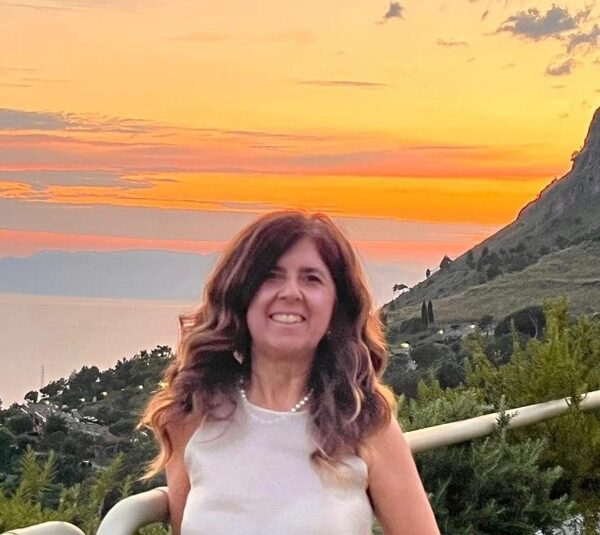 Donna sorridente in camicetta bianca al tramonto dorato su terrazza con vista panoramica collinare e marina