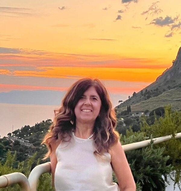 Donna sorridente in camicetta bianca al tramonto dorato su terrazza con vista panoramica collinare e marina