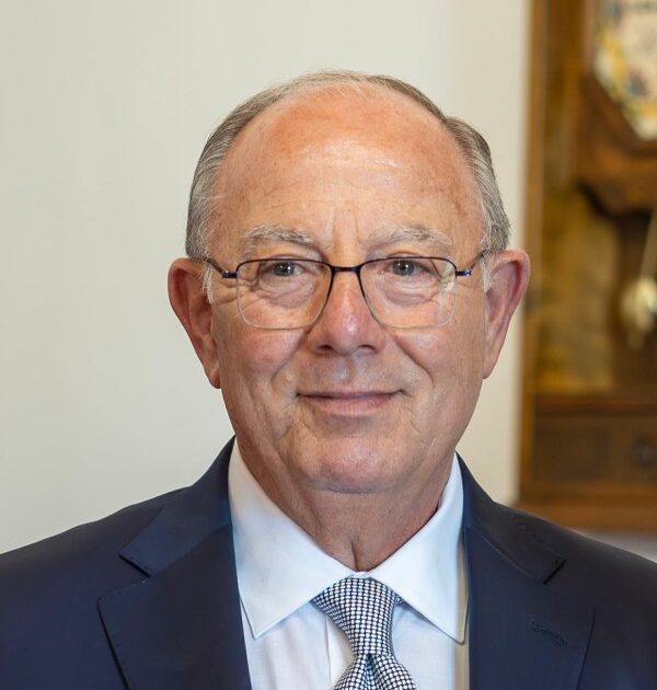 Uomo elegante in completo blu scuro con cravatta grigia e occhiali, ritratto professionale su sfondo architettonico